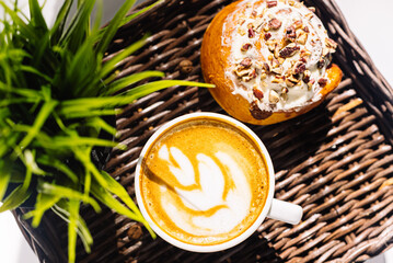 A cup of cappuccino and a cinnamon-nut bun on a wicker tray. .Hard light from the bright summer sun.