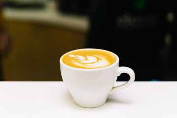 A cup of cappuccino on a white table. Latte art drawn flower on coffee foam.