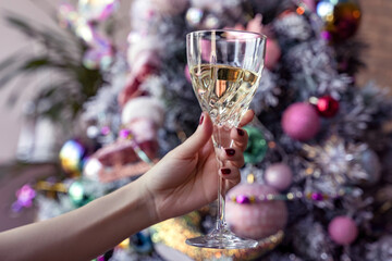 White wine glass in a female hand, woman holding a drink in front of a christmas tree, toast, pink baubles, festive, cheers