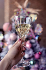 White wine glass in a female hand, woman holding a drink in front of a christmas tree, pink baubles, cheers, toast