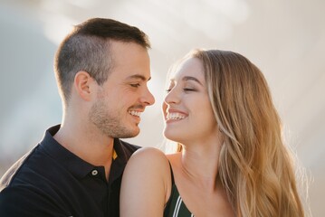 A close photo of couple of tourists who are having fun near a water pool on a date at the sunset in Valencia. A guy is hugging his girlfriend. A girl is sitting on the leg of her boyfriend in Spain