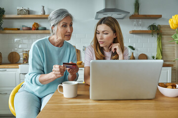 Confident senior woman and her adult daughter using credit card while shopping online from home