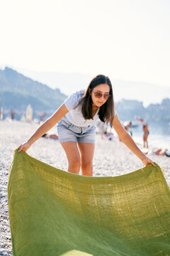 Young Woman Spreads A Blanket On A Pebble Beach