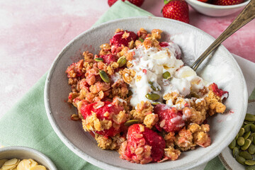 Strawberry crumble with ice cream and almonds in a plate with spoon on green napkin over pink...