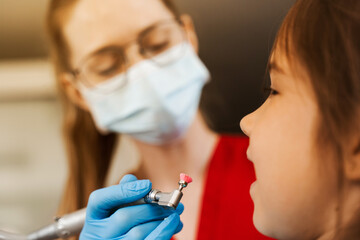 Child dentist makes professional teeth cleaning close-up in dentistry. Professional hygiene for teeth of child in dentistry. Pediatric dentist examines and consults kid patient in dentistry.