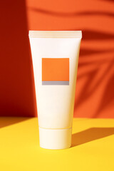 White plastic tube with face, hand and body cream on an orange background with palm leaves shadow. Sun protection lotion, sunscreen. Summer skin care concept with spf. Mockup