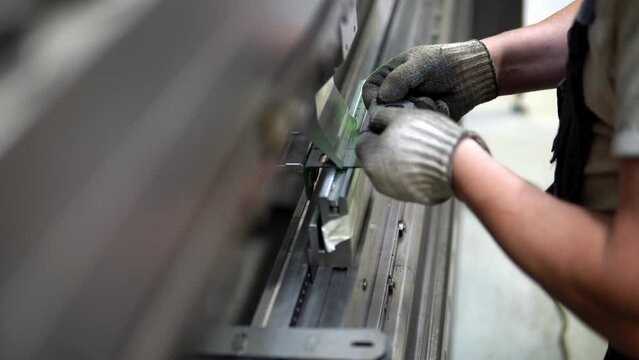 The employee hands are not bending the large parts of the metal on the bending machine, closeup. The CNC operator bending a metal product bends. The employee works at the metal factory.