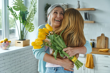 Happy senior woman embracing her daughter and holding a bunch of yellow tulips