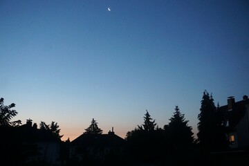 Häuser- und Baumlandschaft vor blauem Himmel mit Mond bei Sonnenaufgang am Morgen im Sommer