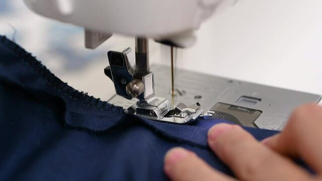 A woman sews a blue fabric on a sewing machine.