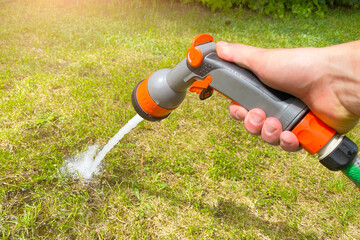 The gardener's hand holds a hose with a sprayer and waters the grass