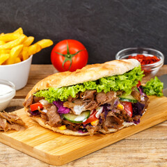 Döner Kebab Doner Kebap fast food meal in flatbread with fries on a wooden board square