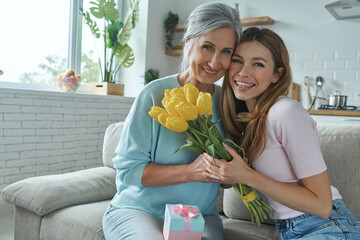 Beautiful senior woman and her adult daughter sitting on the couch and holding bunch of tulips