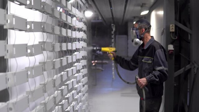 Powder coating of metal products. An employee in a protective mask with a spray gun paints metal parts