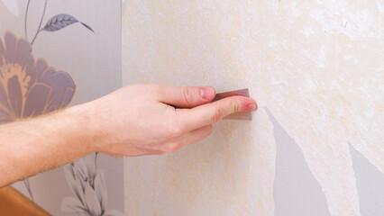 Removing old wallpaper with a spatula and a sprayer with water. A man removes old wallpaper in a...