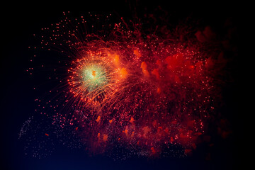 Fototapeta na wymiar A bright firework with a green glowing center and red sparks and smoke flying towards the background of the night sky. High quality photo