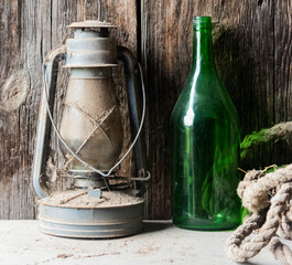 an old kerosene lamp in dust and cobwebs on an ancient wooden chest with a green empty bottle. wooden background.