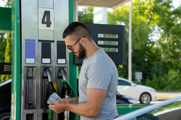 A young man pours gasoline into the gas tank of a white car.A young man pumps gasoline into a gas tank. Fuel and oil crisis. The concept of gasoline prices and the oil crisis.