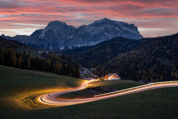 Glowing road at the autumn Dolomite Alps. Amazing landscape with lighting road and snowy mountains on background at San Genesio village location, Province of Bolzano, South Tyrol, Italy