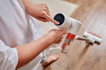 Women hands and display control wireless portable vacuum cleaner in the kitchen. A woman cleans the...