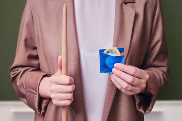 Woman teacher holding a condom in her hands on school blackboard in the classroom