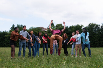 Young man doing a flip with his friends of different ethnicities supporting him