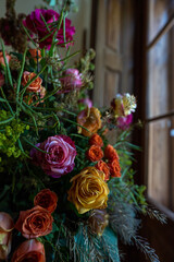 lots of multicoloured roses in wooden ( cork ) vases, bouquet of roses in a room on table in a historical building, vintage window, wedding decoration concept