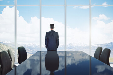 Back view of young man standing in modern meeting room interior with reflections on table, chairs...
