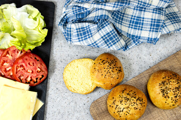 Hamburger preparing, sheet of soft cheese and slice of tomatoes and salad on black board with burger bun
