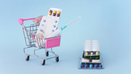 Pills, tablets and syringe a shopping cart on a blue background
