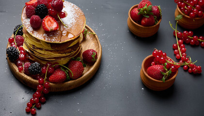 Obraz na płótnie Canvas A stack of pancakes with fresh fruits poured with syrup on a black background