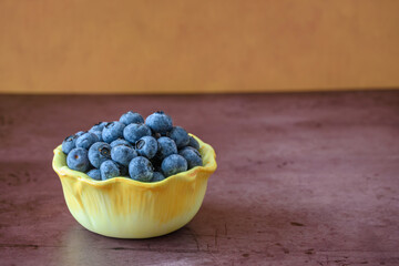 Fresh picked organic blueberries in a flower shaped bowl on a dark and moody rustic background, tasty and nutritious
