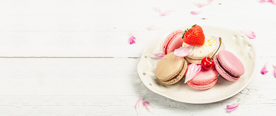 Macarons with strawberries, cherries and peonies flower petals, on a white wooden background