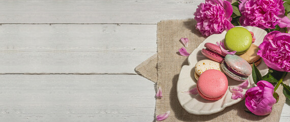 Macarons with a bouquet of peonies on white wooden background. Sweet dessert, pastel colors