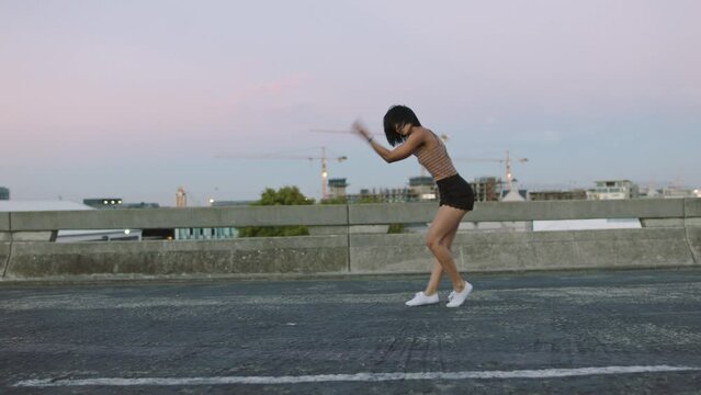 Young woman dances alone on empty street. Stylish and funky dancer performs freestyle in a deserted urban environment. Hip hop artist practicing her moves and enjoying a wild and free lifestyle