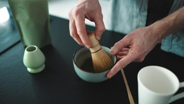 Men's hands stirring with a bamboo whisk the matcha in the bowl indoors