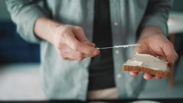 Male hands spreading cottage cheese on the bread in the kitchen at home