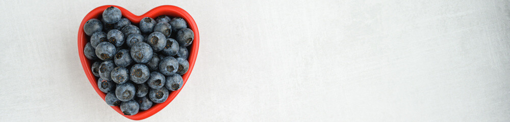 Fresh picked organic blueberries in a heart shaped bowl on a gray background, tasty and nutritious
