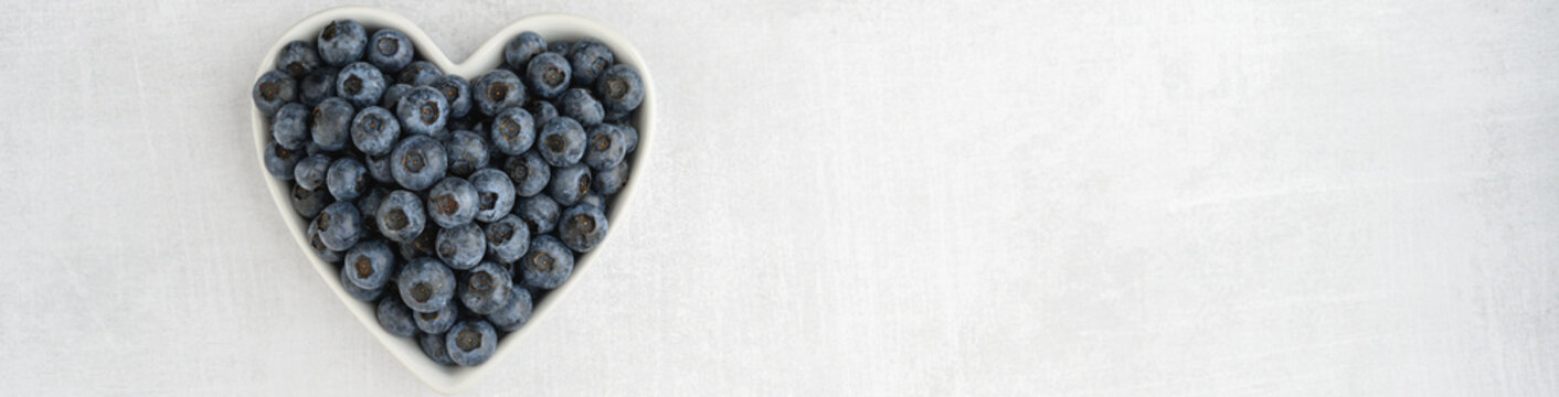 Fresh picked organic blueberries in a heart shaped bowl on a gray background, tasty and nutritious
