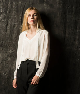 portrait of a beautiful blonde woman with long hair in a white blouse and black trousers on a gray isolated background.a charming girl posing on a dark background.