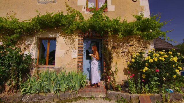 French morning in Provence near Paris. A girl in a white dress walks on the threshold of a French old house with a cup of coffee and a croissant