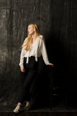 Fototapeta premium portrait of a beautiful blonde woman with long hair in a white blouse and black trousers on a gray isolated background.a charming girl posing on a dark background.