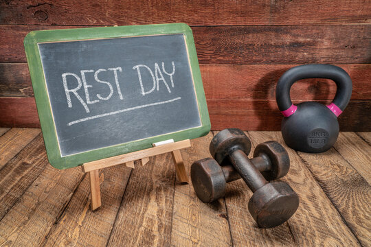rest day - message or reminder, white chalk writing on a slate blackboard with dumbbells and kettlebell, fitness and recovery concept