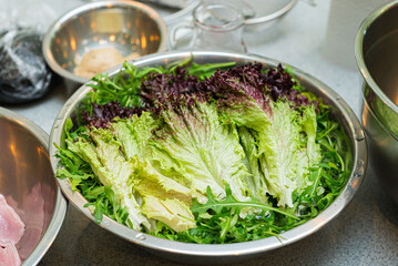 A bowl of washed arugula leaves and lolla rossa..Wet lettuce leaves ready to cook