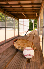 Baseball with glove on dugout bench with blurred background - obrazy, fototapety, plakaty