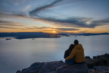 Couple of tourists enjoy the sunset over Titicaca lake from Amantani island, Puno - Peru.