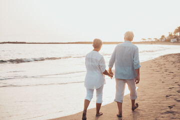 Couple of old mature people walking on the sand together and having fun on the sand of the beach enjoying and living the moment. Two cute seniors in love having fun..