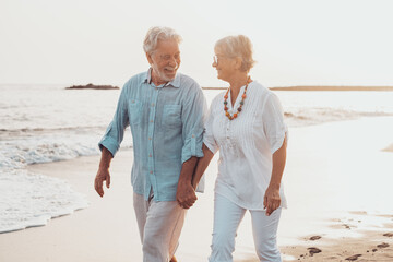 Couple of old mature people walking on the sand together and having fun on the sand of the beach enjoying and living the moment. Two cute seniors in love having fun. Barefoot walking on the water.