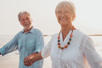 Couple of old mature people walking on the sand together and having fun on the sand of the beach enjoying and living the moment. Two cute seniors in love having fun. Barefoot walking on the water.
