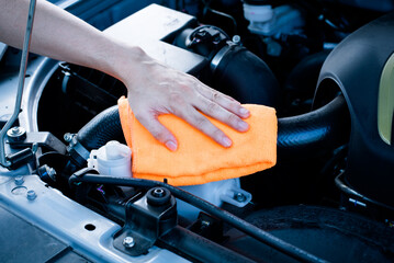 Wipe cleaning the car engine with orange microfiber cloth